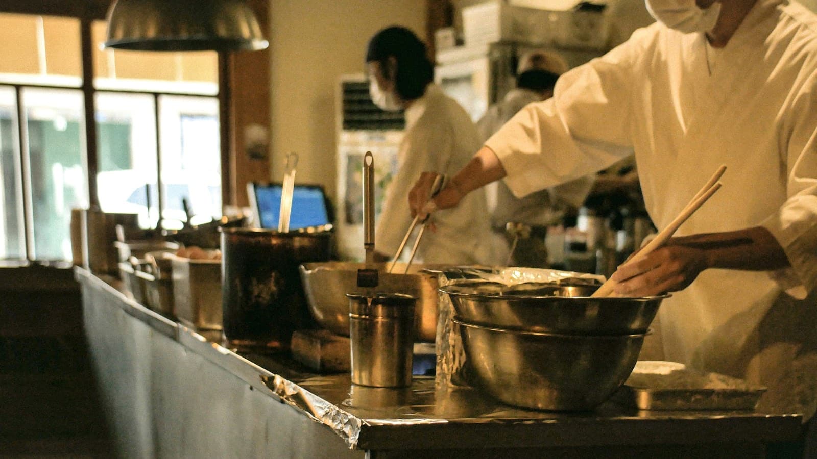 Cooks in white uniforms working at a steel counter in a busy restaurant kitchen
